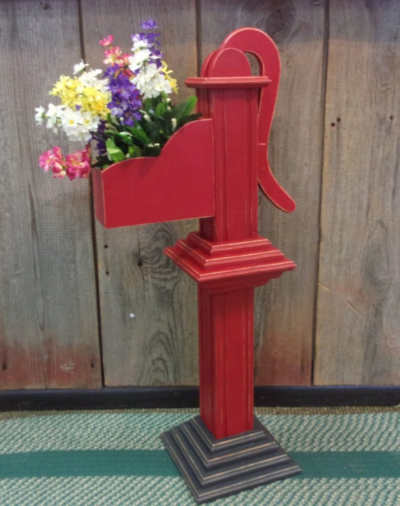 Wooden hand pump painted red and shown with flowers